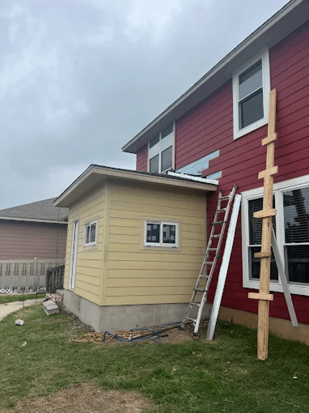 Yellow-sided home addition under construction with extension ladder against the wall