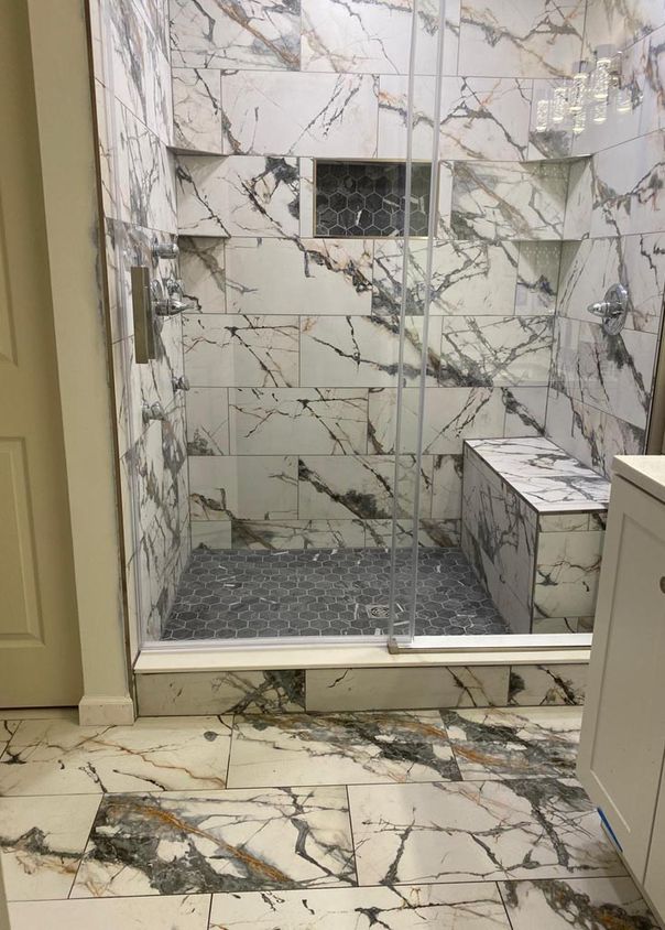 Walk-in marble shower with glass enclosure, hexagon mosaic floor, and matching marble bathroom floor