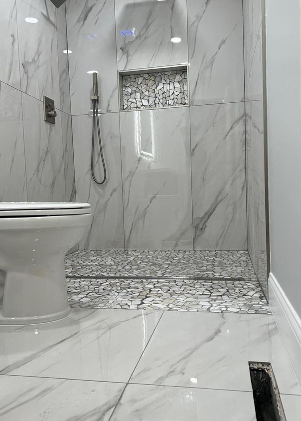 Marble-look tile bathroom with walk-in shower, recessed niche, and pebble floor inlay
