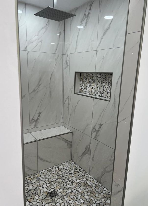 Marble-look tile shower with pebble mosaic floor, built-in bench, and rainfall showerhead
