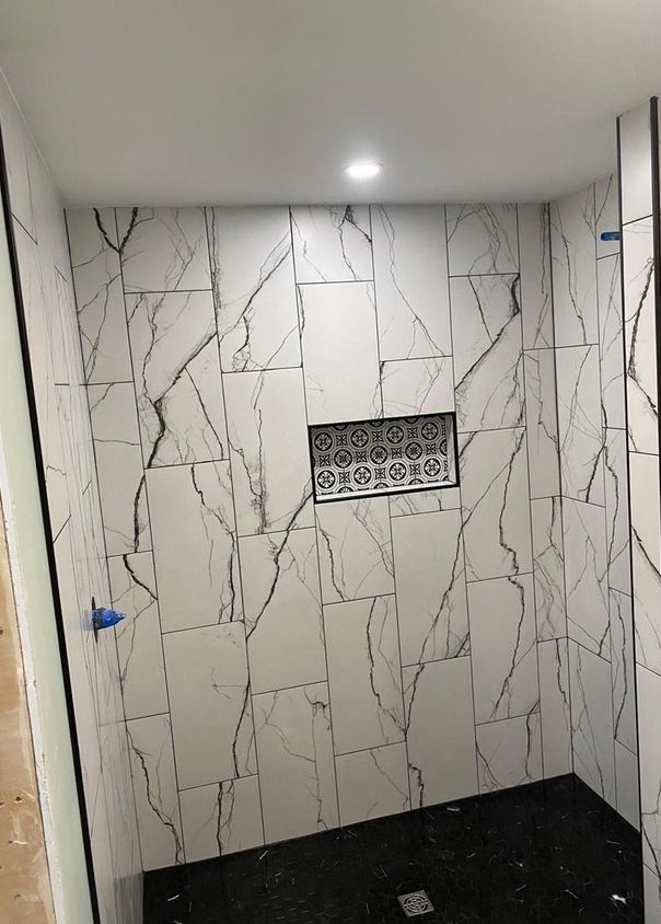 White marble-look tile shower with decorative cement-tile niche and black tile floor
