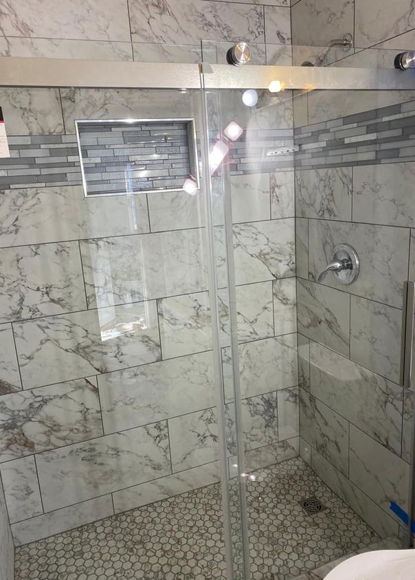 Marble-look tile shower with glass sliding door, mosaic accent stripe, and hexagon floor