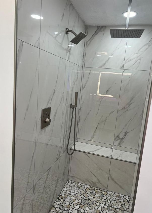 Marble shower with rainfall showerhead, matte black handheld fixtures, and pebble floor