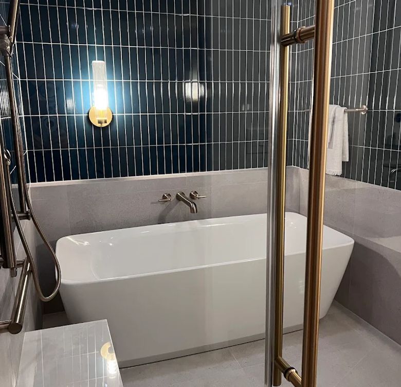 Freestanding bathtub with dark blue vertical subway tile accent wall and brass fixtures